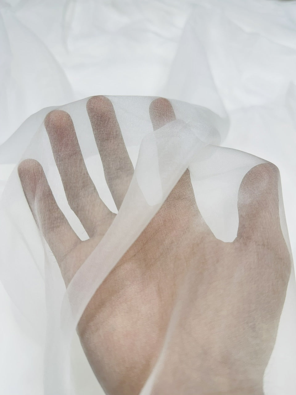 Hand wearing sheer white organza fabric on a light background