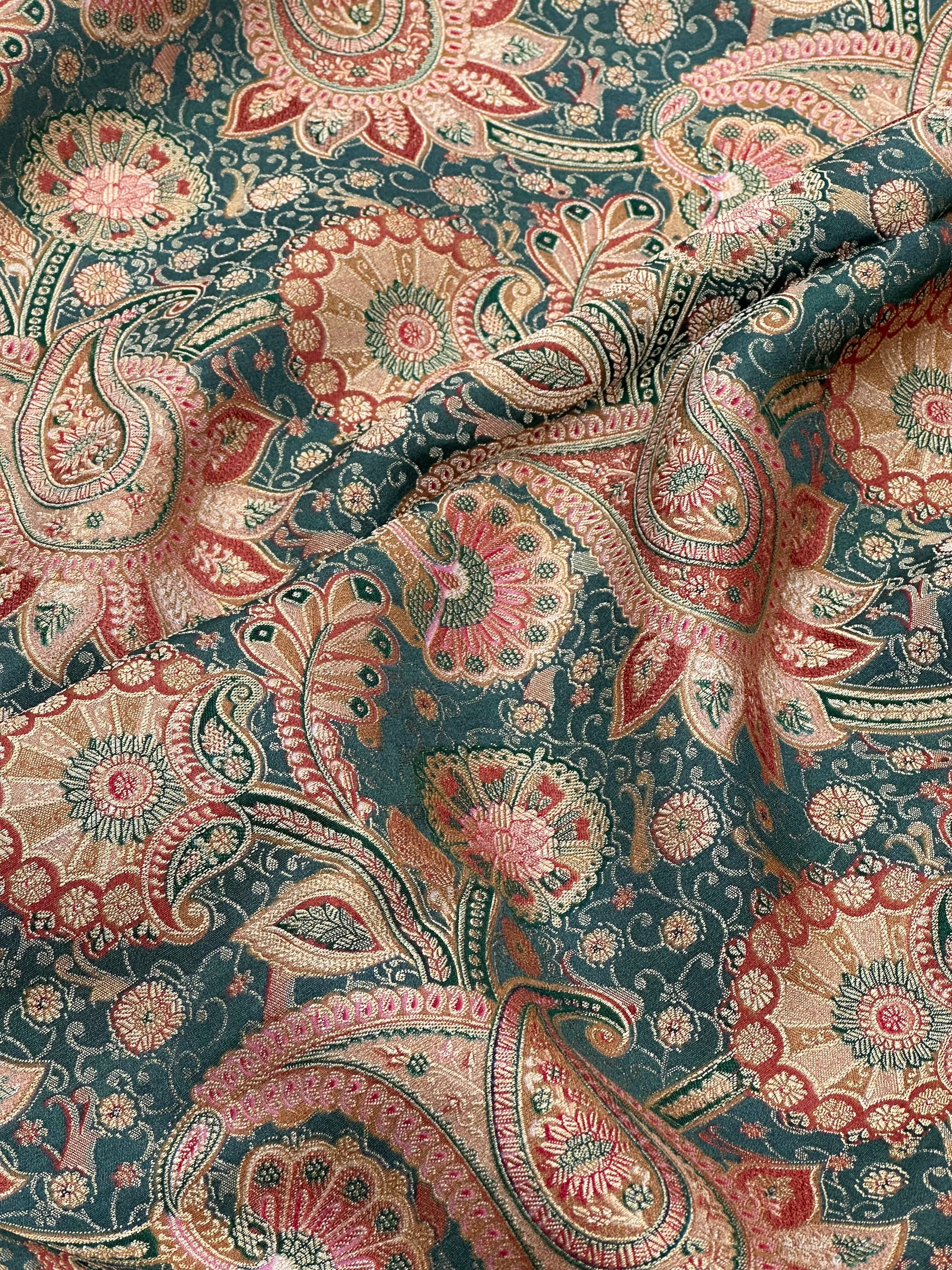 Close-up of a patterned fabric with paisley design in green, red, gold, and beige.