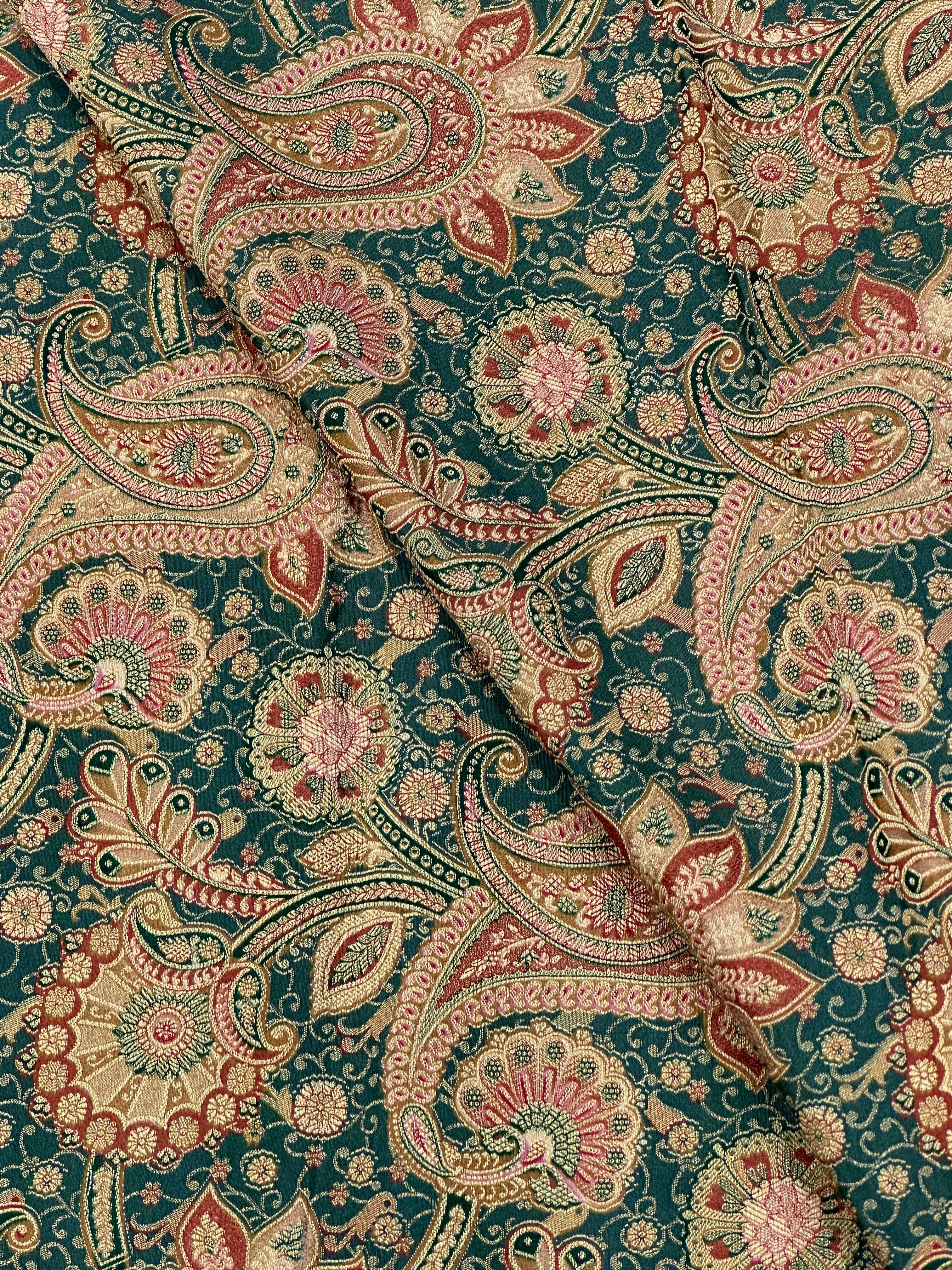 Patterned fabric with paisley design in red, beige, and gold on a dusty green background