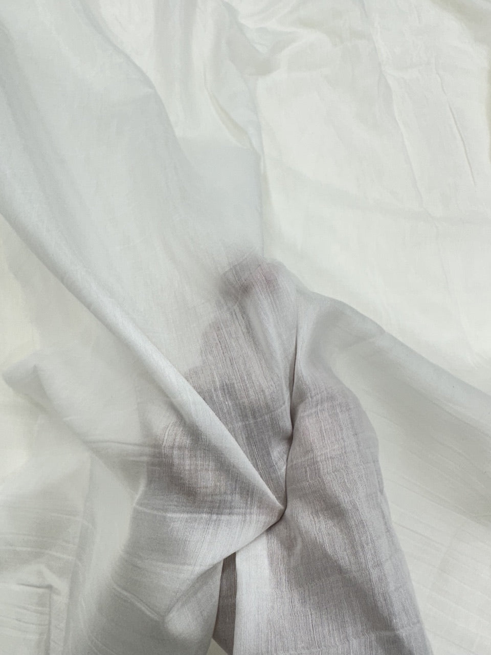 Close-up of hand holding white mul Chanderi fabric with subtle texture