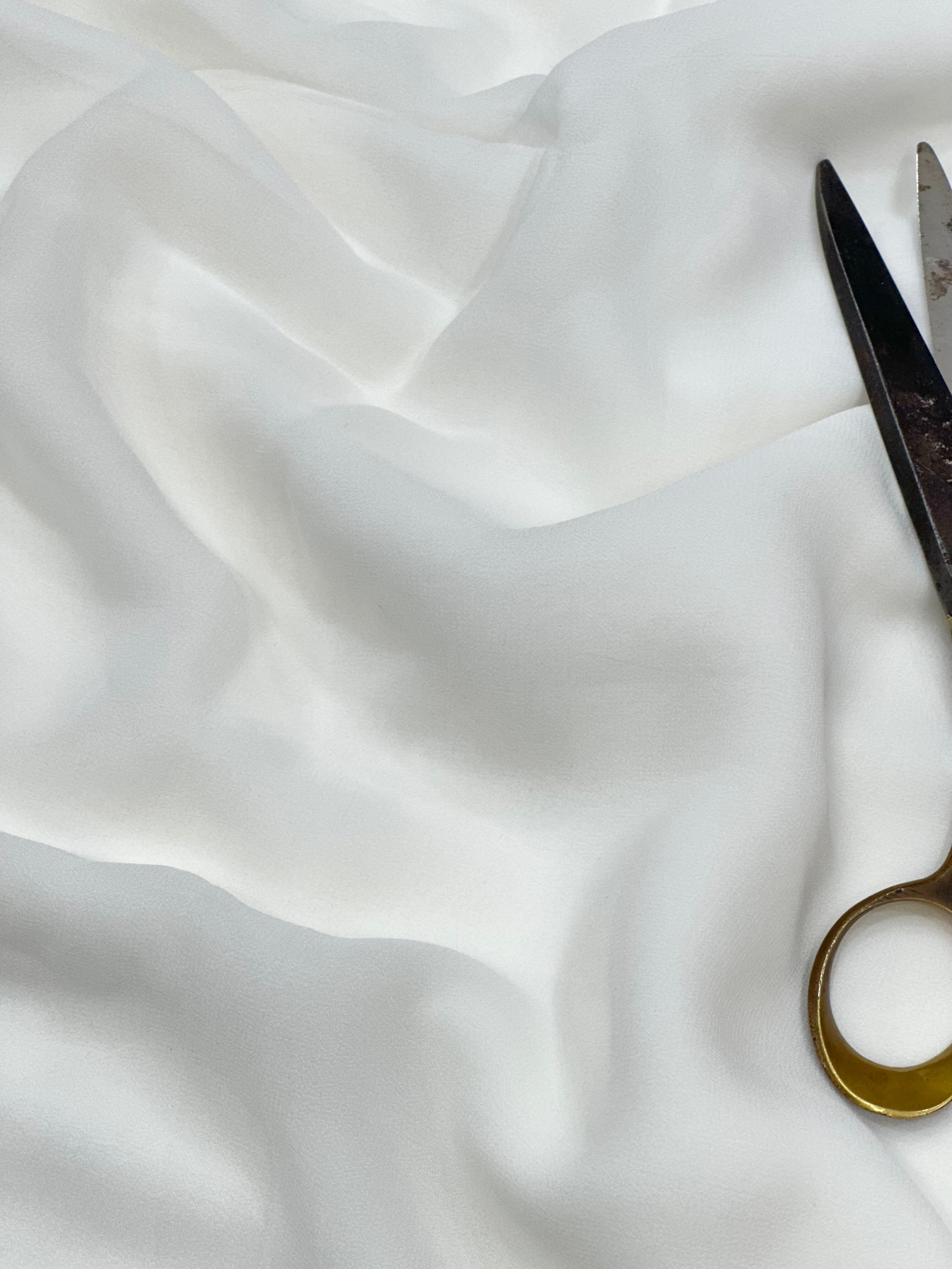 Pair of scissors on a white georgette fabric background