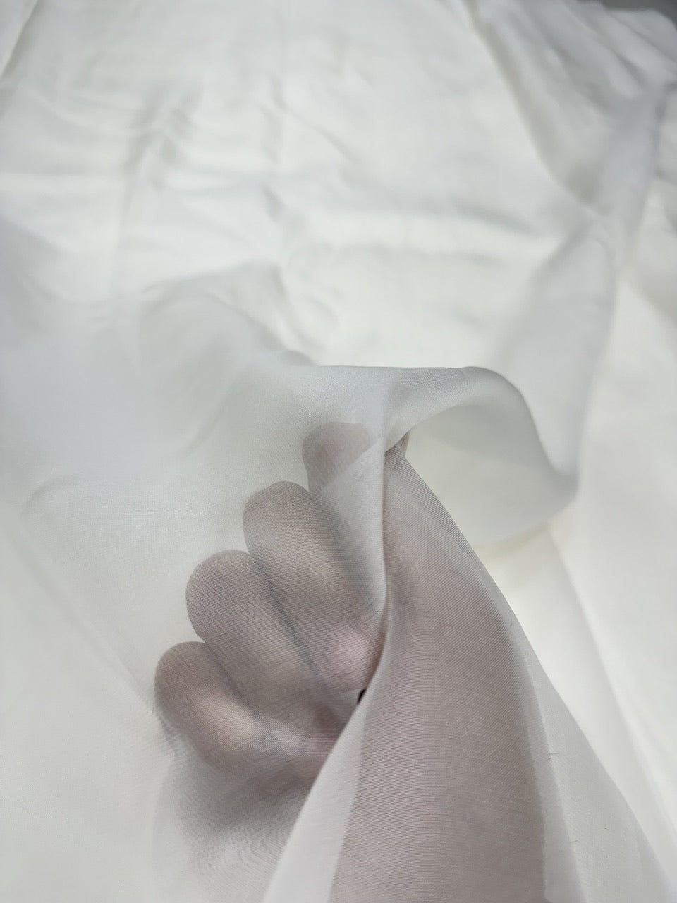 Close-up of a hand holding a white organza fabric against a white background