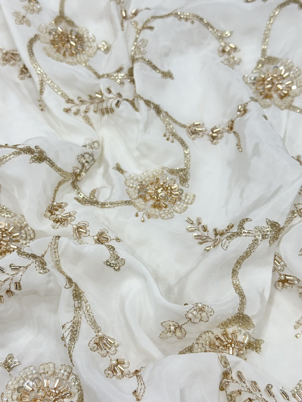 Close-up of white crepe fabric with intricate gold handwork beads embroidery