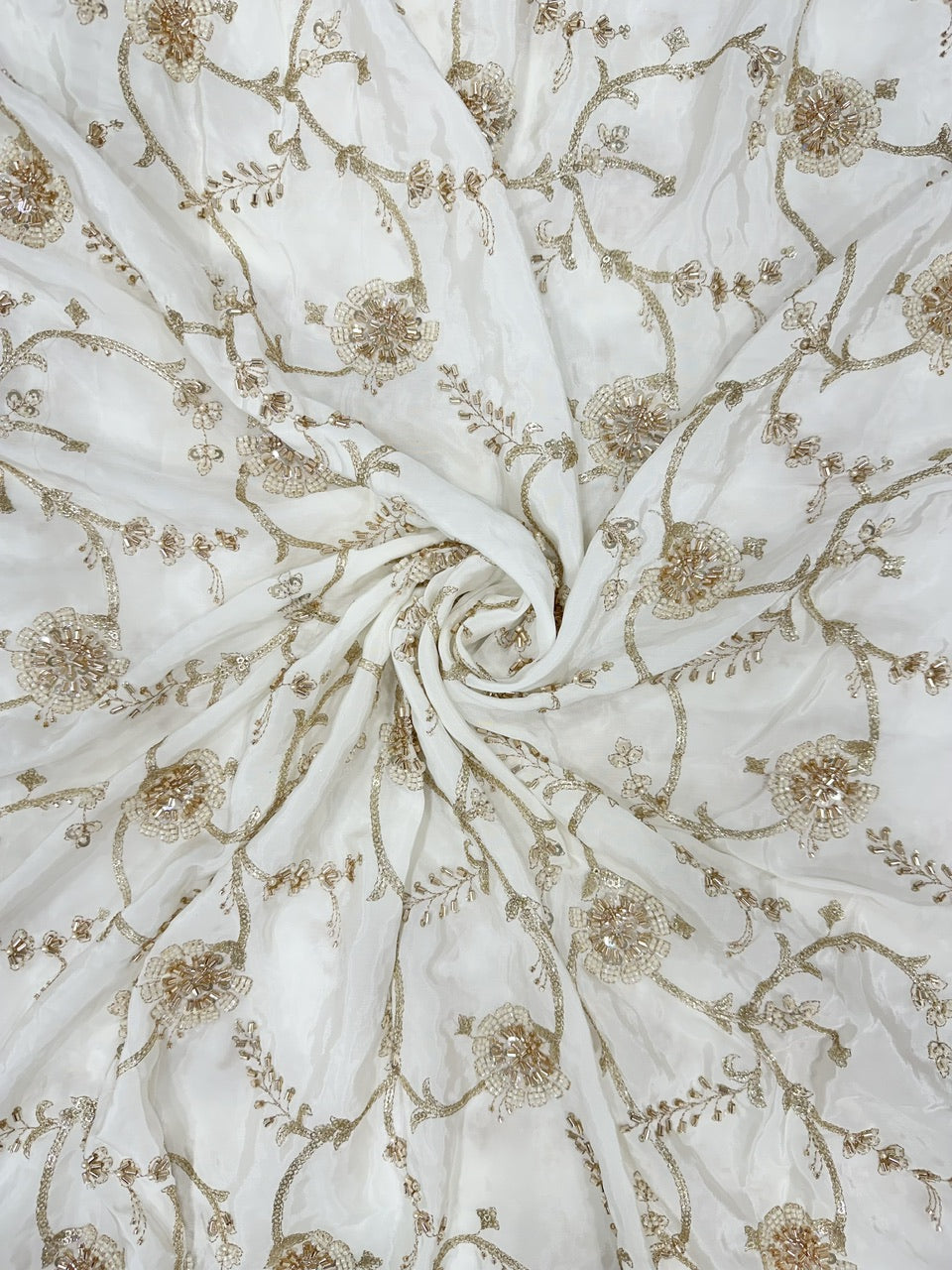 Close-up of white crepe fabric with gold floral handwork pattern