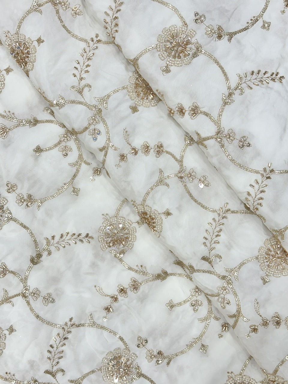 Close-up of beads embroidered natural crepe fabric with gold floral patterns on a white background