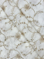Close-up of beads embroidered natural crepe fabric with gold floral patterns on a white background