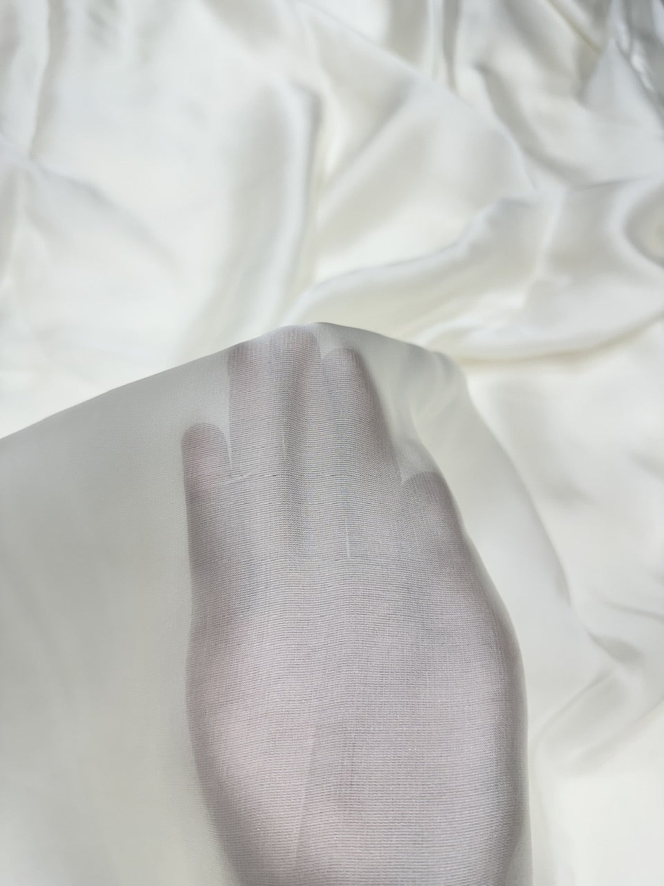 Close-up of white fabric with a hand on a white organza satin showing texture