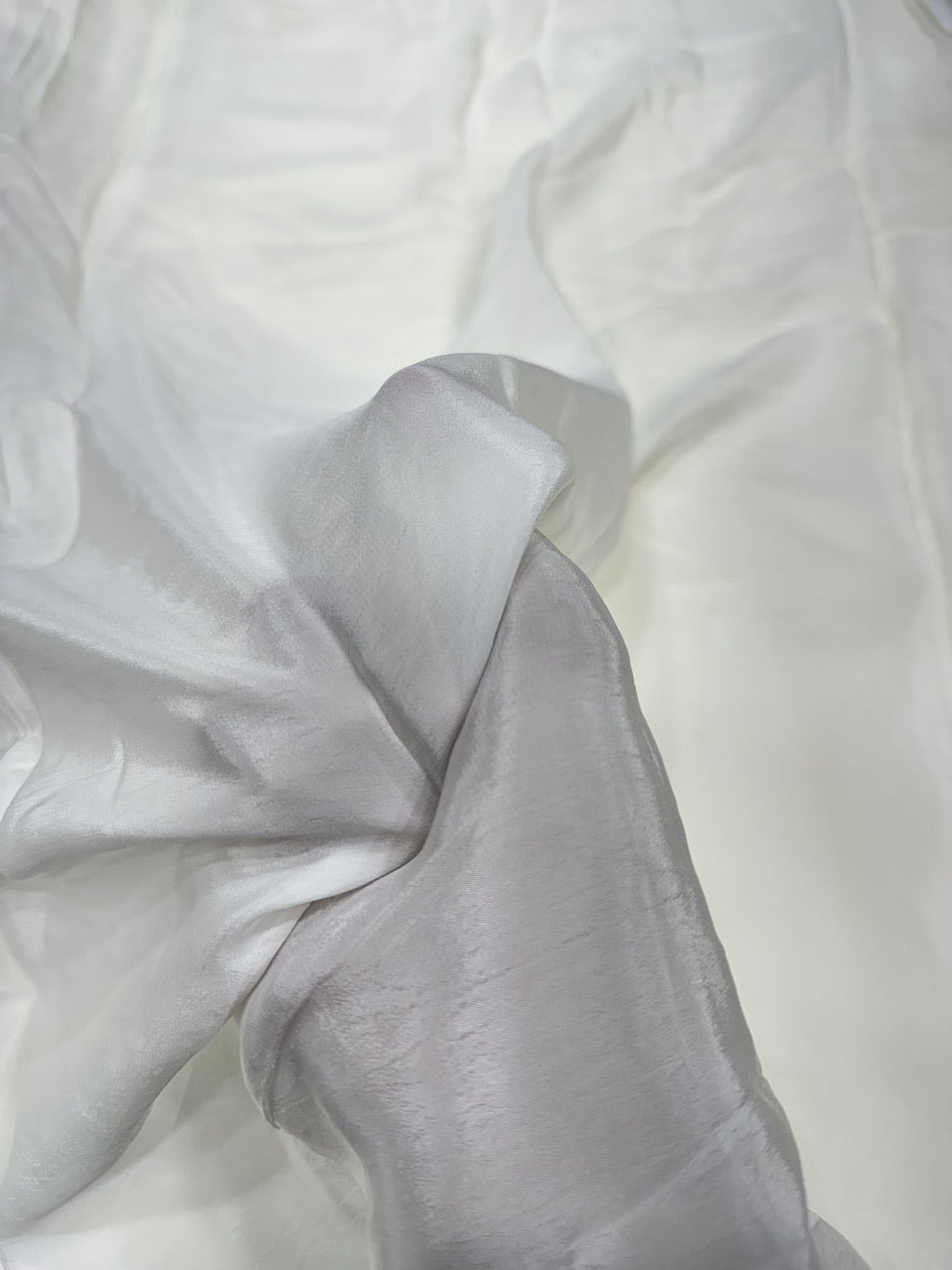 Close-up of white crepe fabric with folds with a hand holding the fabric