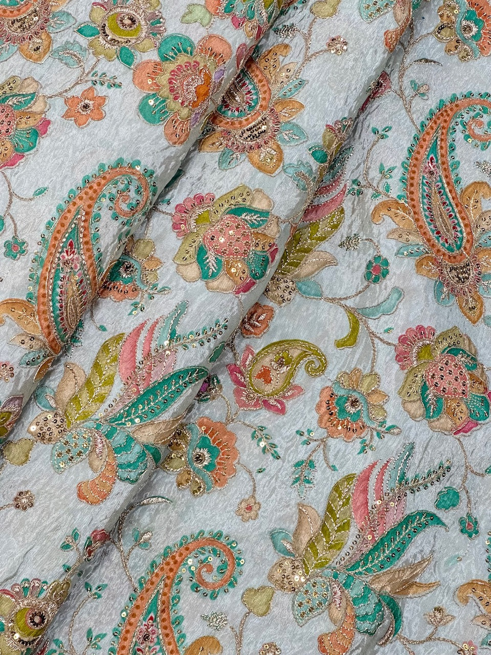Close-up of a fabric with intricate paisley and floral patterns in multicolors on a light background.