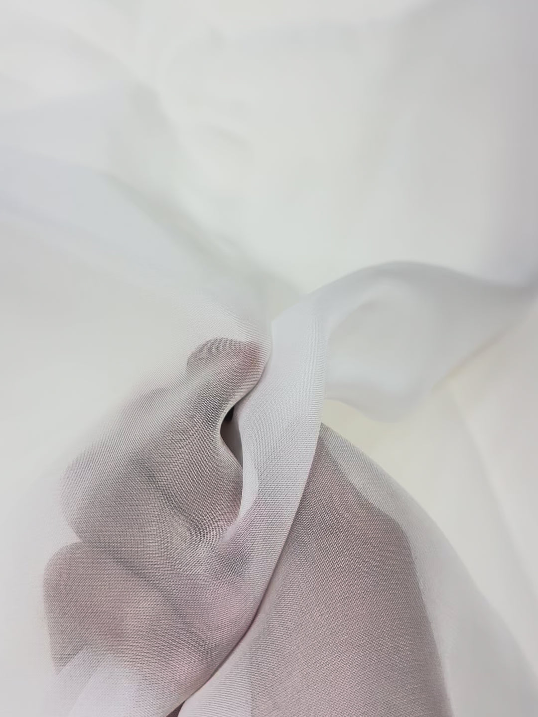 Close-up of a hand holding a white organza fabric against a white background